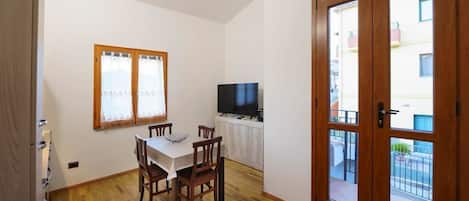 A dining area with a table and chairs, a television, and a sliding glass door leading to an outdoor balcony.