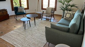 Een woonkamer met een bank, twee stoelen, een bijzettafeltje, een lamp en een potplant.