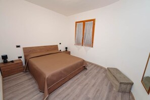 Ein Schlafzimmer mit einem hölzernen Bett, einem Nachttisch mit Lampe, einer kleinen Holzbank und einem Fenster mit Vorhängen.