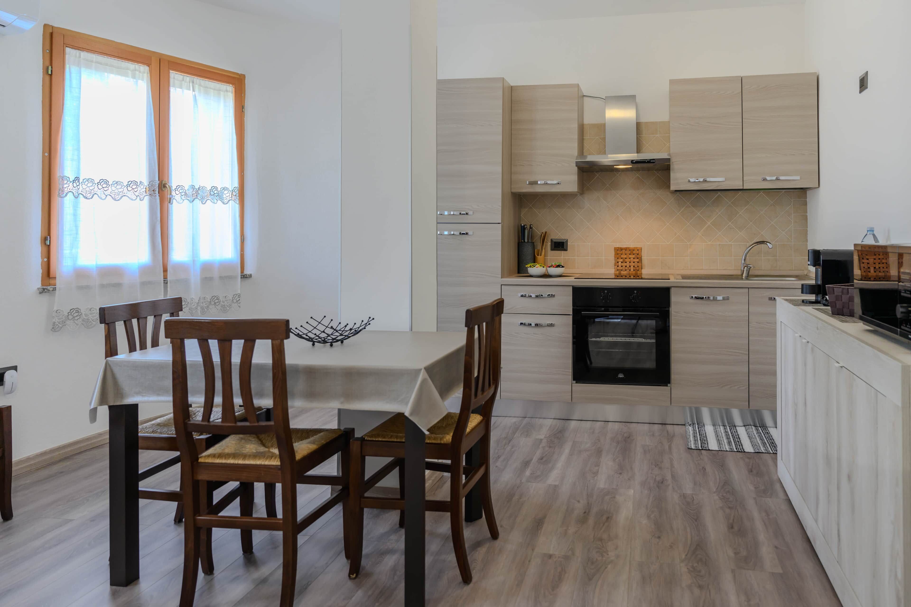 Una cocina moderna con armarios de madera clara, horno empotrado y un comedor con mesa y sillas.
