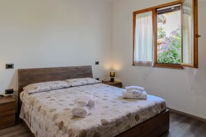 A single bed with a patterned bedspread, a bedside lamp, and a window with a view of flowers. - Casa vacanze Sibilla appartamento Scirocco (Villa San Pietro)