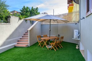 A patio with a table and chairs, a covered umbrella, and a staircase leading to a balcony. - Casa vacanze Sibilla appartamento Scirocco (Villa San Pietro)