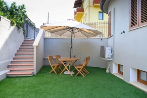 Une terrasse avec une table et des chaises, un parasol blanc et un escalier.