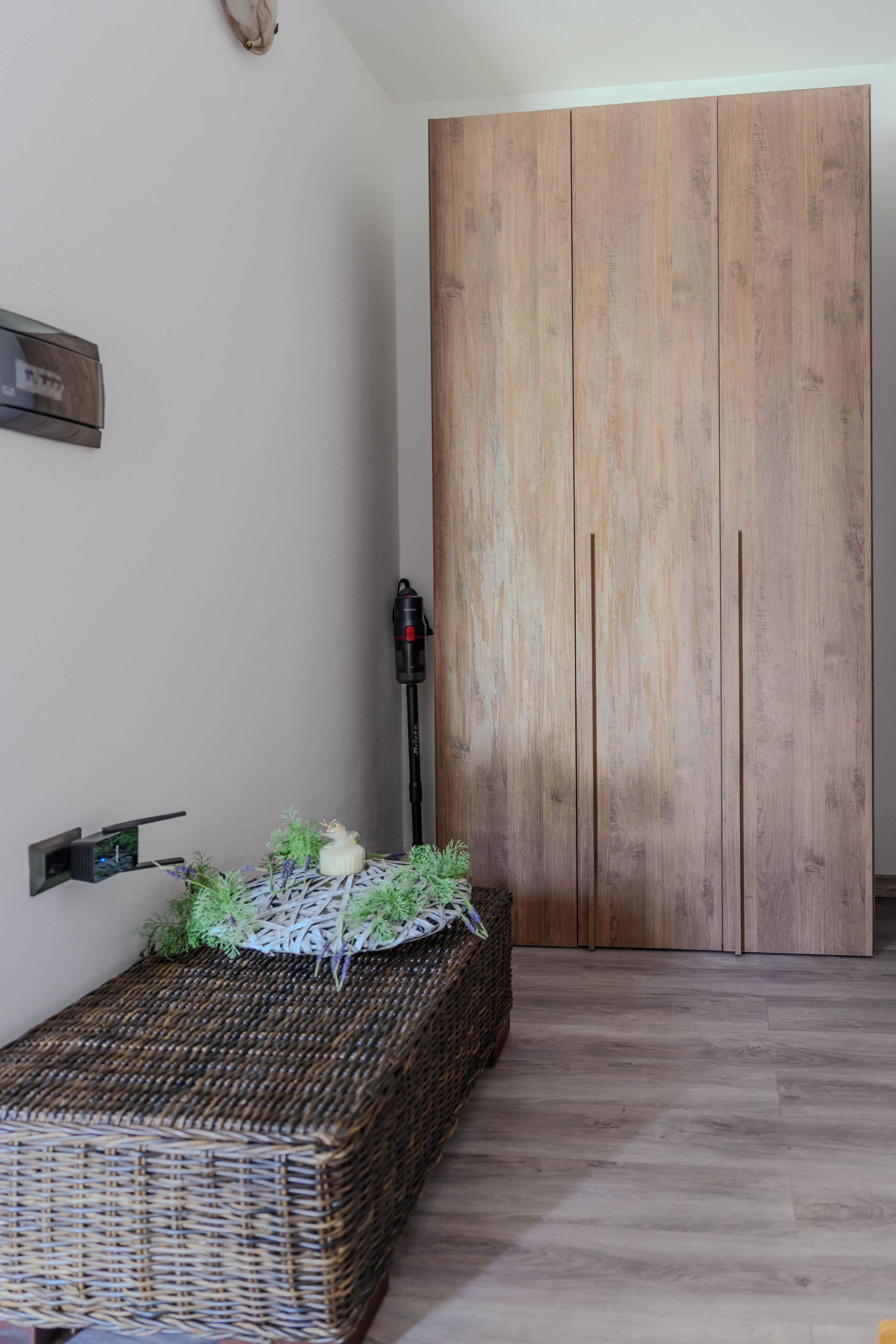 Une pièce avec une armoire en bois, un banc en osier agrémenté d’une plante et une étagère fixée au mur.