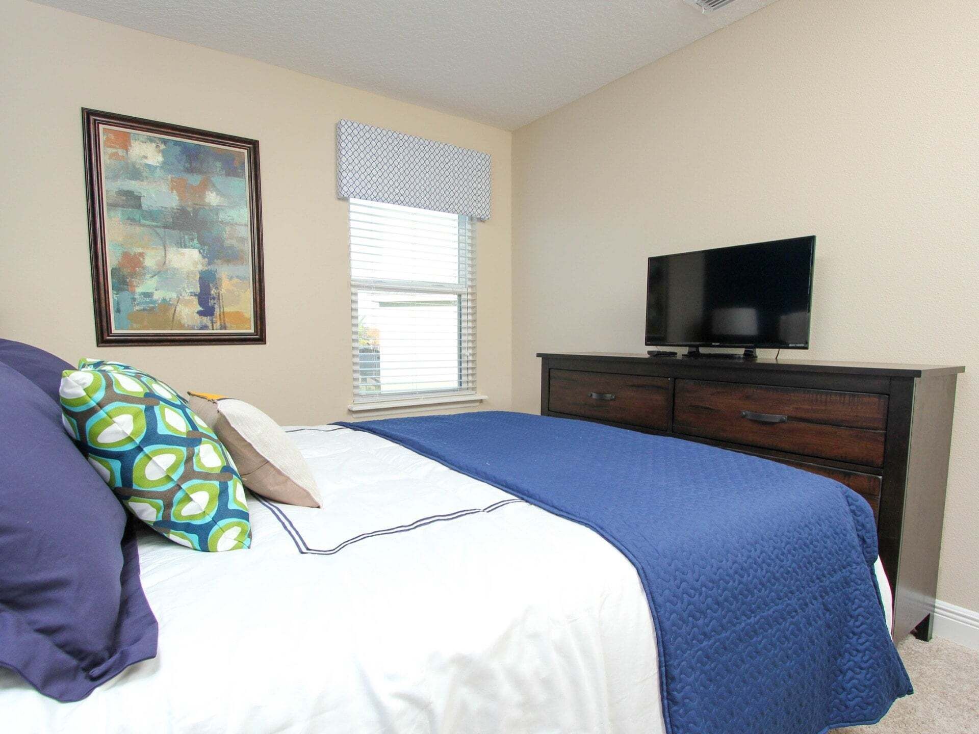 A bedroom with a bed, a dresser, a television, a window with blinds, and a painting on the wall.