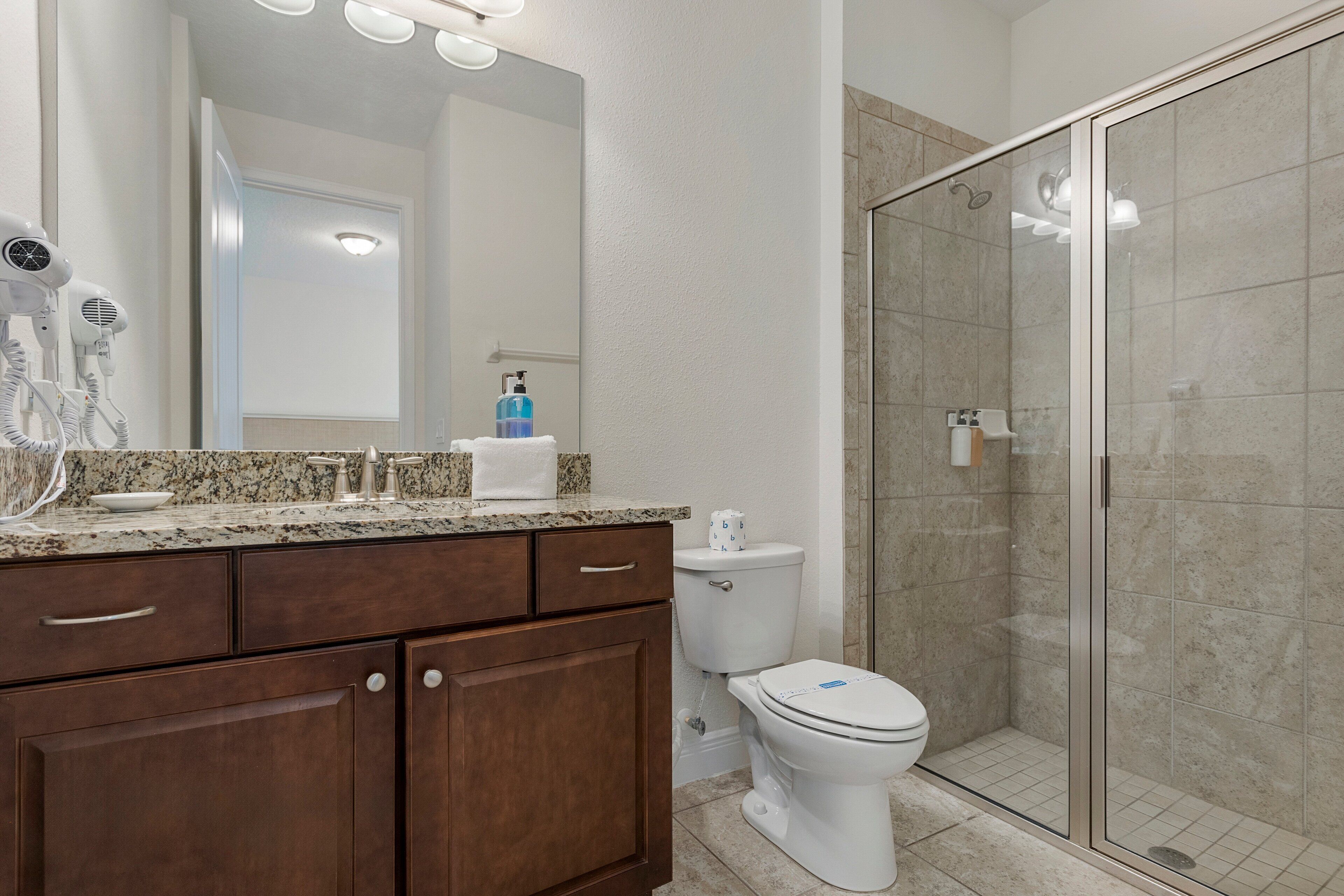 A bathroom with a granite countertop, a white toilet, a glass shower enclosure, and a dark wooden vanity.