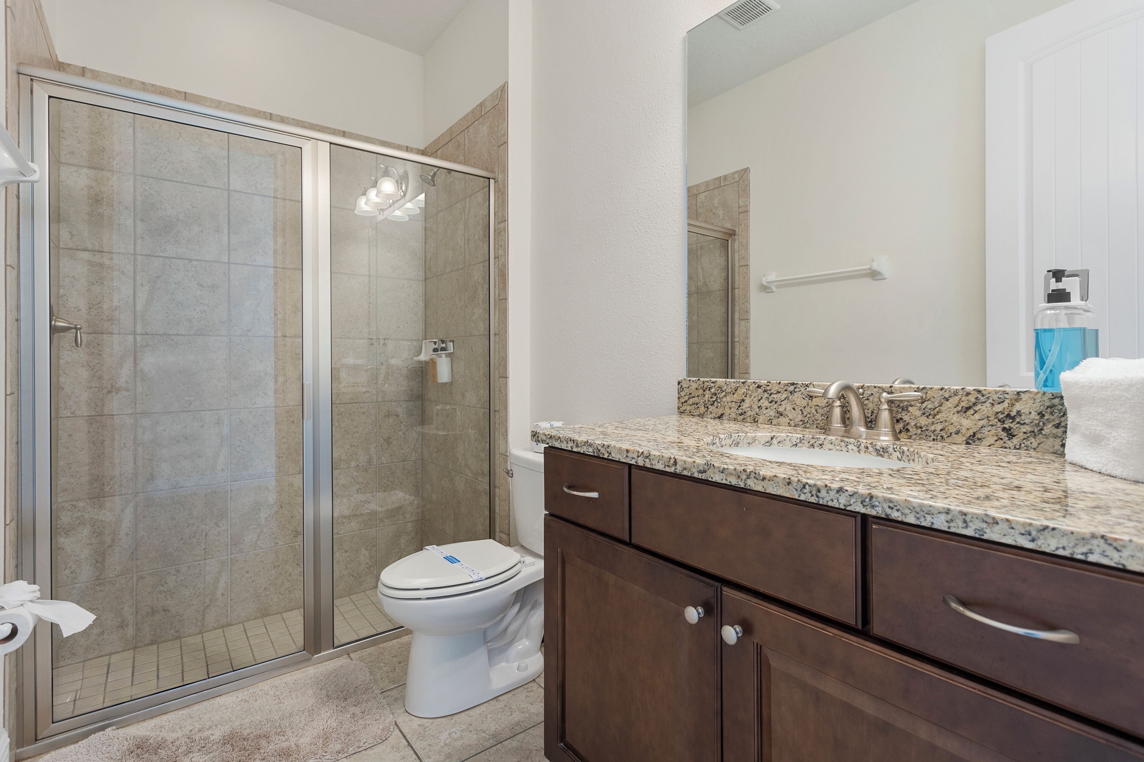 A bathroom with a glass shower enclosure, a white toilet, a granite countertop, and a large mirror.