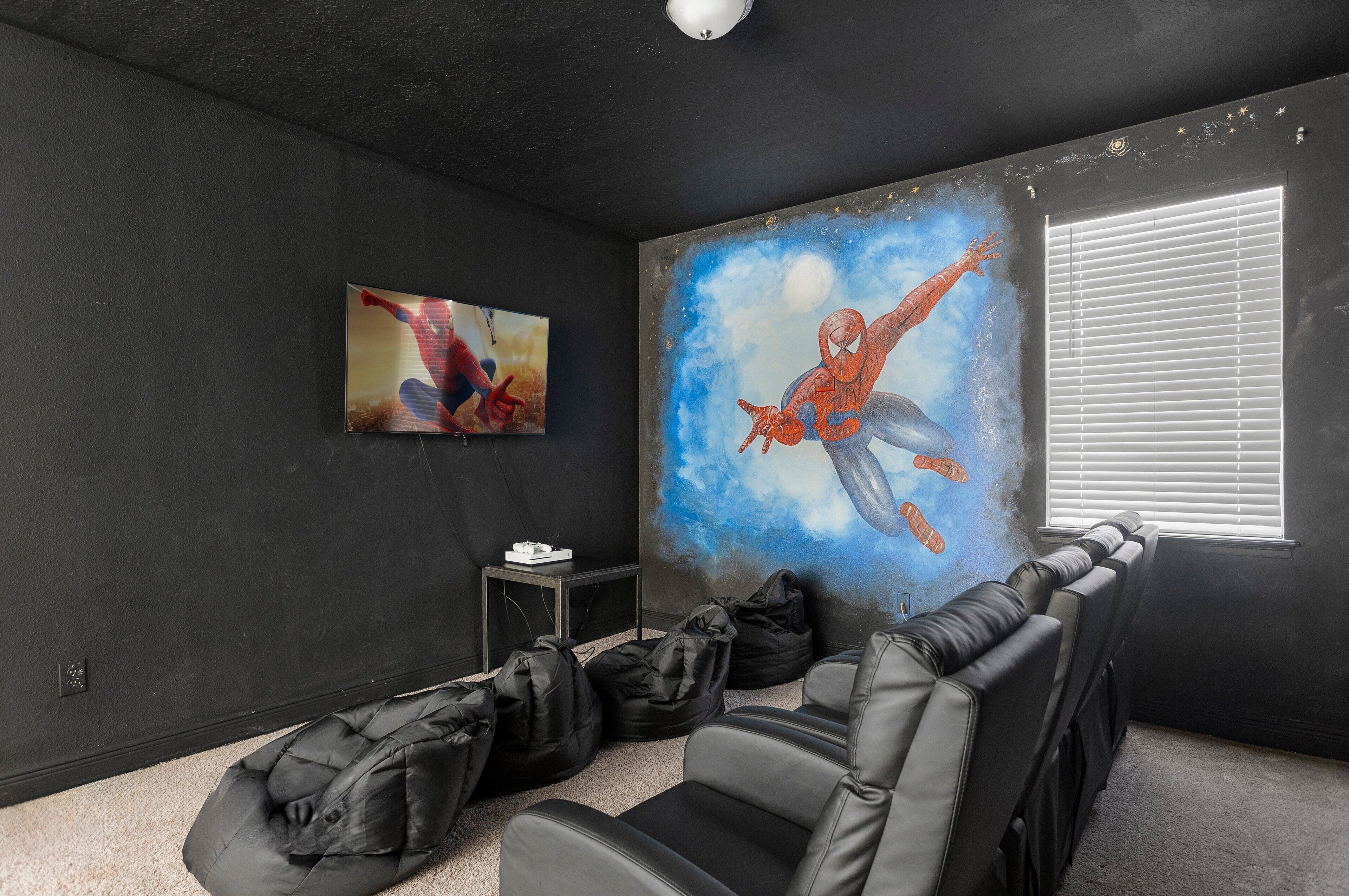 A dark-themed room with a large Spiderman mural, black leather seating, and a projector screen.