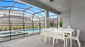 Un espacio exterior techado con piscina, mobiliario blanco y vistas a casas vecinas.