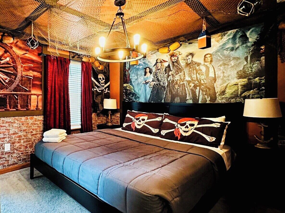 Une chambre avec un grand lit, une fresque représentant des pirates sur le mur et un lustre.