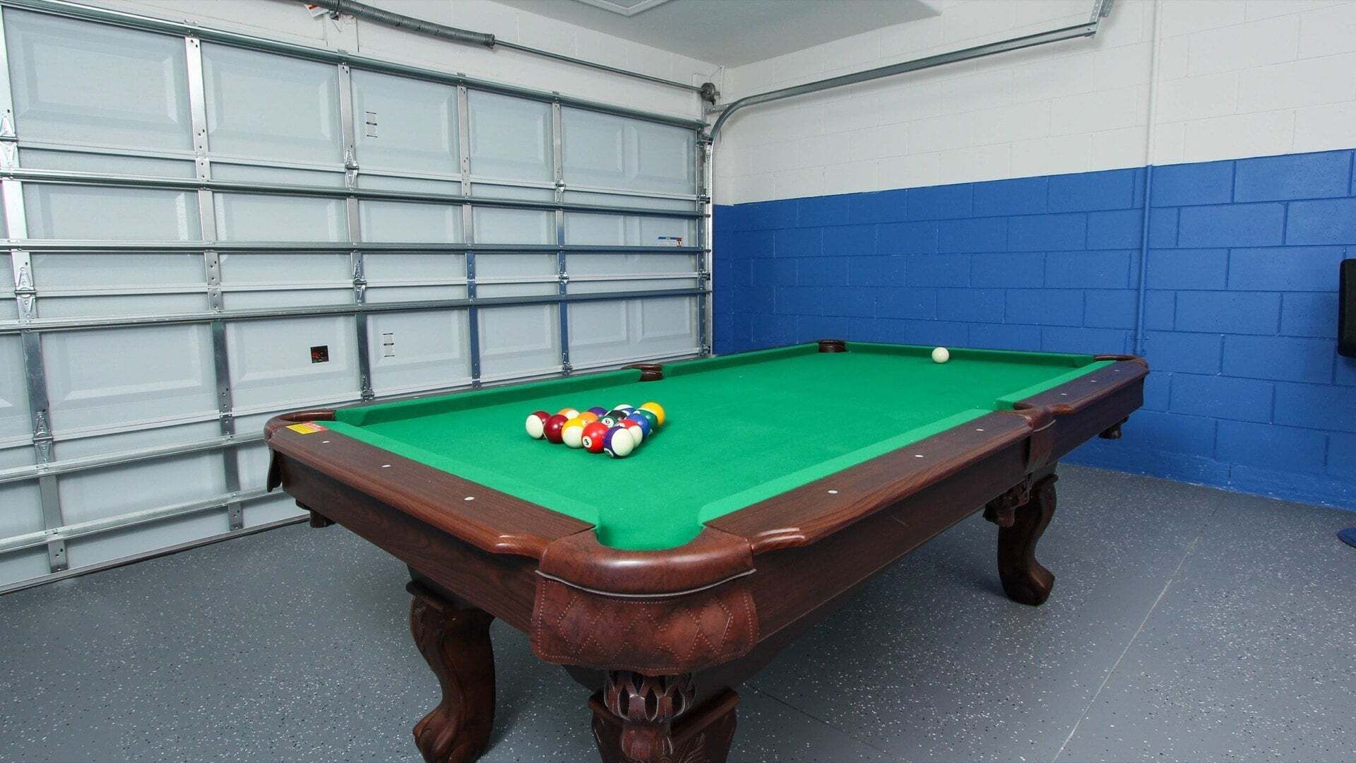 A pool table with balls in a room with a garage door and blue walls.