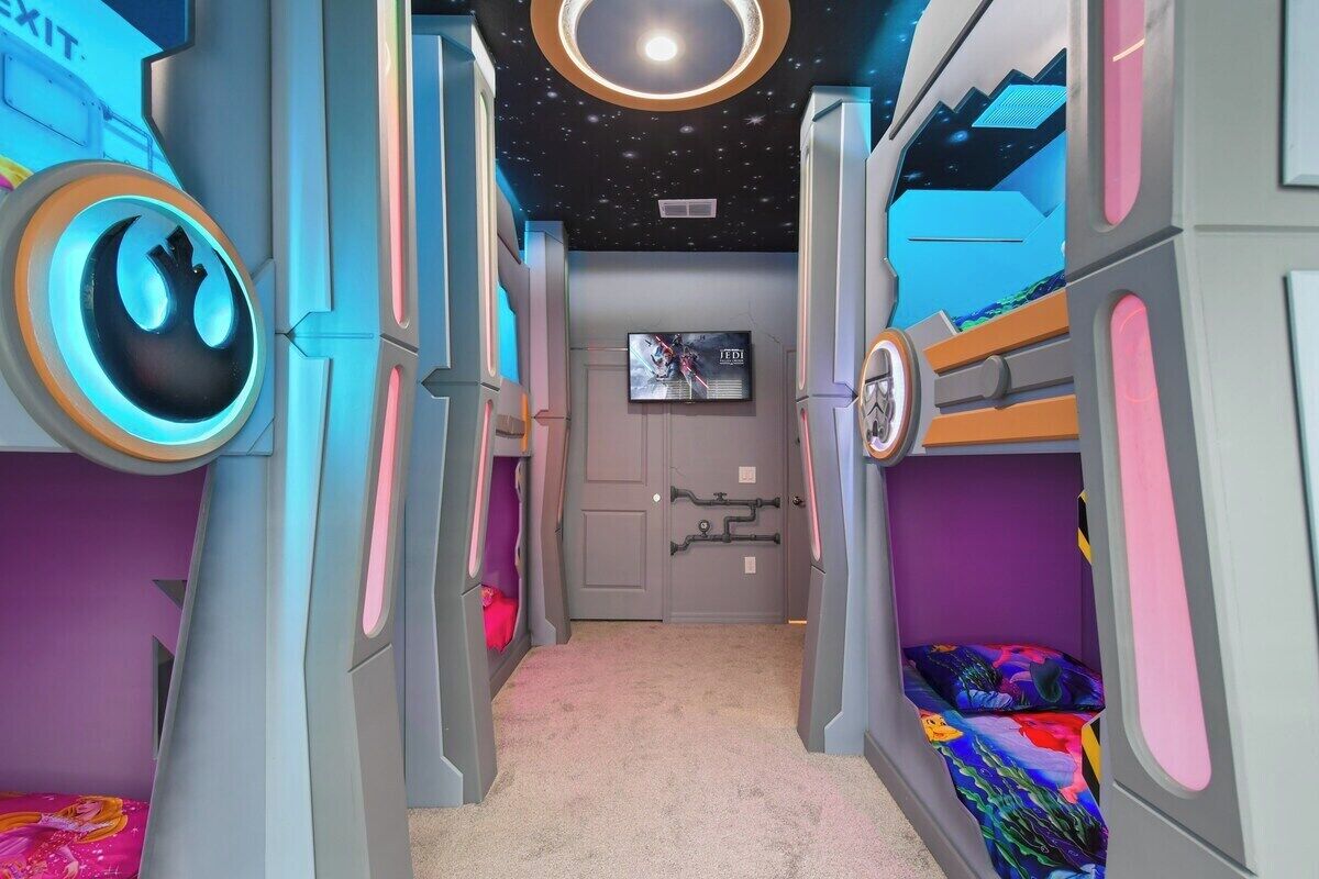 A children's room with bunk beds, a ceiling starry design, and a TV on the wall.