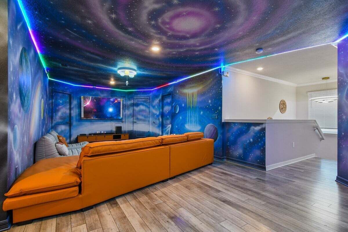 A room with a galaxy-themed mural, a wooden floor, and a sofa.