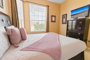 Ein Schlafzimmer mit Bett, Kommode, Fernseher und einem Fenster mit Jalousien.