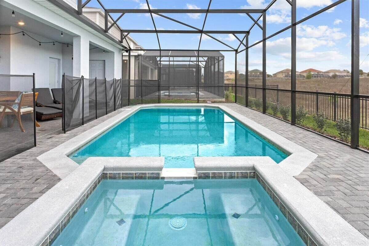 Une piscine rectangulaire à l’eau d’un bleu limpide, entourée d’une terrasse couverte dotée d’une structure métallique et offrant une vue sur le paysage.