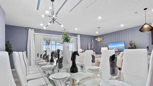 A modern dining area with glass tables and white chairs, a large window with curtains, and a television on the wall. - 2190lc · Amazing 10br Themed/windsor Island/free Waterpark (Davenport)