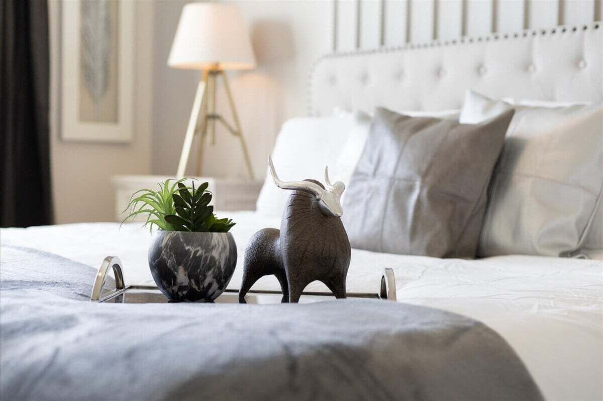Un lit bien fait, recouvert d’une couverture grise, avec une plante en pot et deux figurines d’animaux décoratives posées sur le lit.