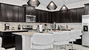 A modern kitchen with dark cabinetry, a central island with bar stools, a stainless steel refrigerator, and pendant lighting. - 2190lc · Amazing 10br Themed/windsor Island/free Waterpark (Davenport)