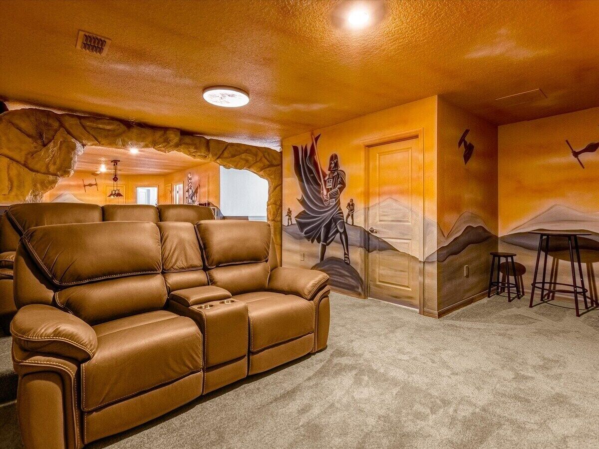 A home theater room with a reclining leather couch, a wall mural, and a bar area.