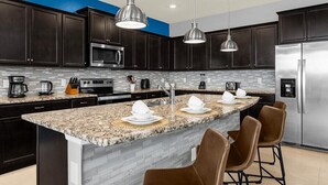 A modern kitchen with dark cabinets, a granite countertop, stainless steel appliances, and a central island with bar stools. - 3739la · Brand New 10br/pool/spa/ Disney Fireworks View (Davenport)