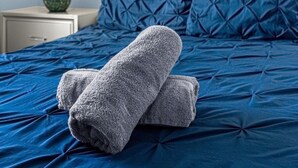 Ein ordentlich gemachtes Bett mit blauer Bettwäsche und einem Paar gefalteter Handtücher.