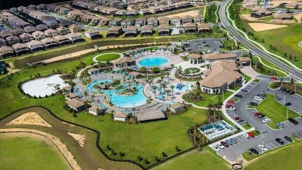 Luftaufnahme eines Resorts mit mehreren Schwimmbecken, einem Hauptgebäude und einem Parkplatz.