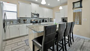 A modern kitchen with white cabinets, granite countertops, and a central island with bar stools. - 5424 Solterra Circle, Davenport,5beds (Davenport)