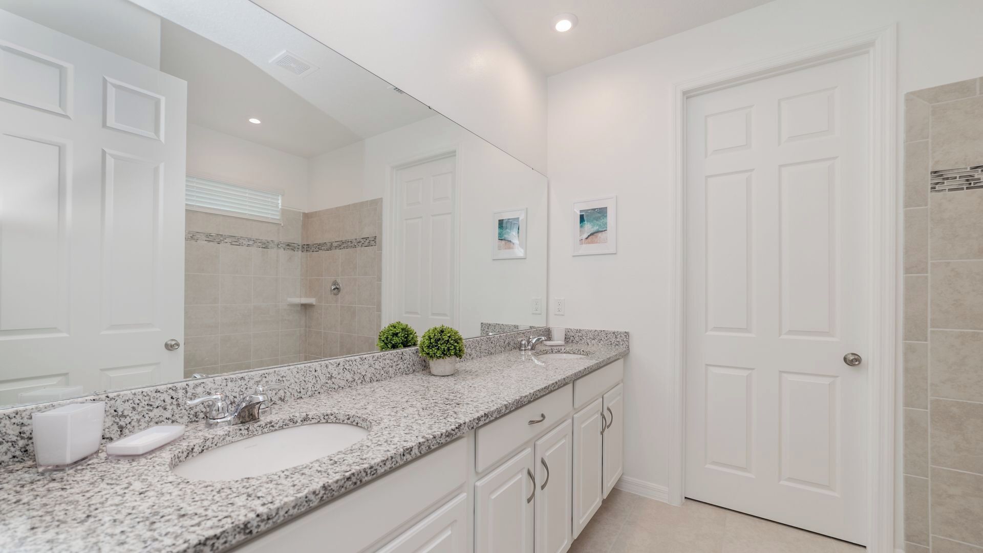 Une salle de bain moderne avec un grand miroir, deux lavabos, une douche et une porte.