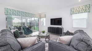 Ein modernes Wohnzimmer mit grauen Sofas, einem Glastisch und einem an der Wand befestigten Fernseher.