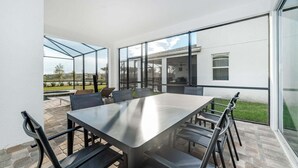 Ein moderner Essbereich im Freien mit großem Tisch und Stühlen, großen Fenstern und Blick auf Pool und Gartenlandschaft.
