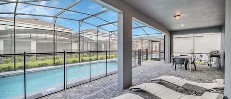 Et overdækket område med swimmingpool, liggestole og et terrassebord.