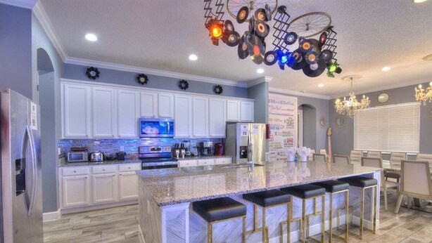 A modern kitchen with white cabinets, a granite island with bar stools, and a unique ceiling light fixture. - 4011-ol-music Genres Themed With Bowling Alley (Davenport)
