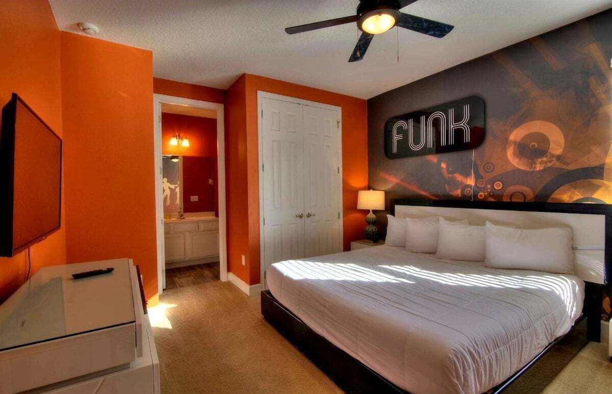 A bedroom with a bed, a ceiling fan, a wall-mounted TV, and a door leading to a bathroom.