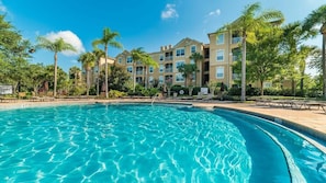 A swimming pool with clear blue water, surrounded by palm trees and a multi-story building with balconies. - Alm2774-204 (Kissimmee)