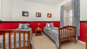 Slaapkamer met twee houten bedden, een nachtkastje en een raam met geruite gordijnen.