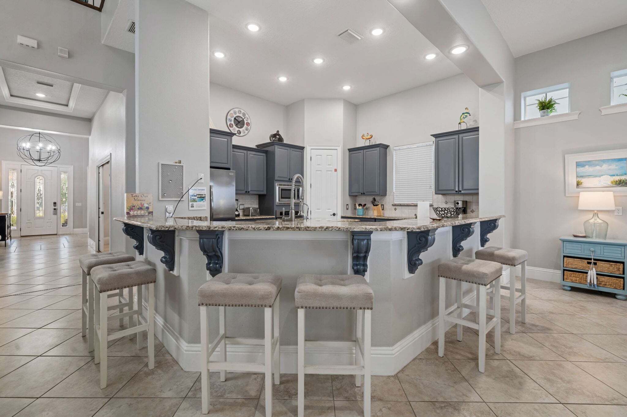A kitchen with a central island, bar stools, and a dining area with a chandelier.