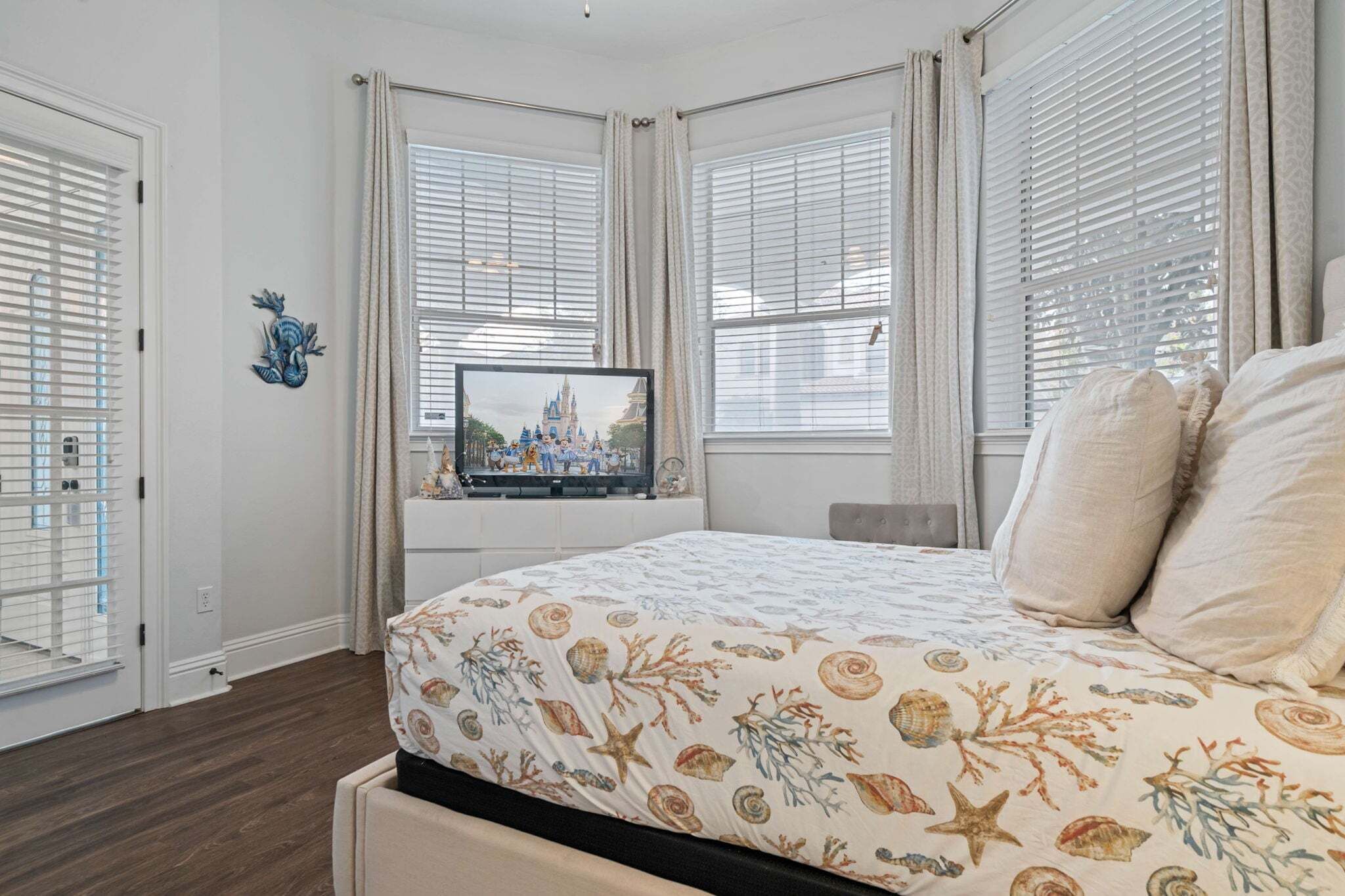 Une chambre à coucher avec un lit, un téléviseur posé sur un meuble et une fenêtre avec des stores.