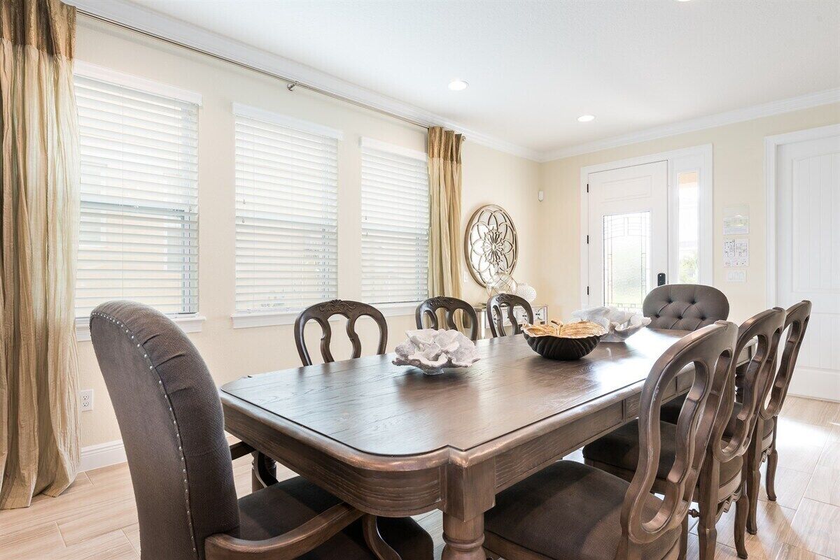 A dining room with a wooden table and six chairs, a decorative wall piece, and a window with blinds.
