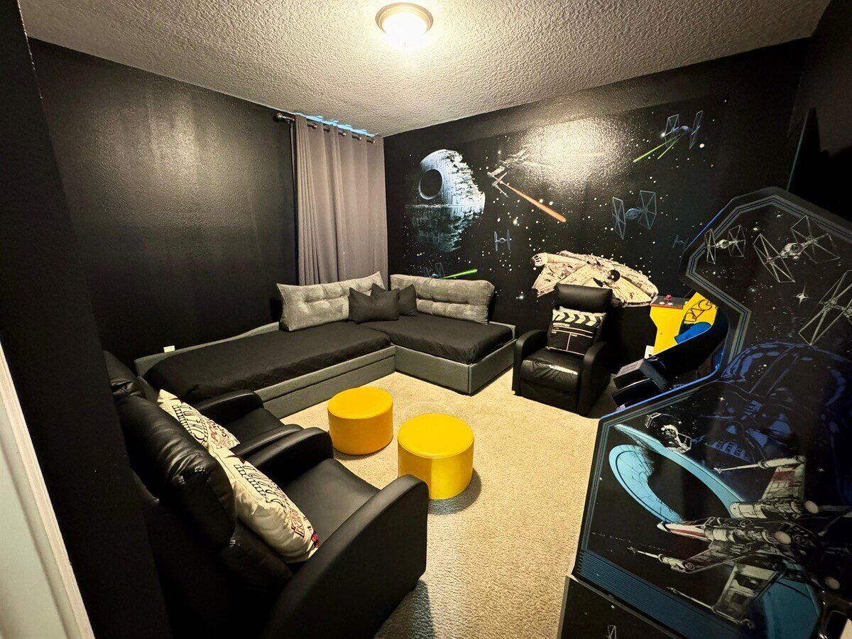 Una stanza con un divano componibile, due pouf gialli, una parete a tema Star Wars e una lampada a soffitto.