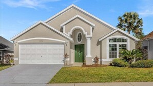 A single-story house with a beige facade, a green front door, and a white garage door. - 15730 BAY Vista Drive Clermont, 4bed (Clermont)