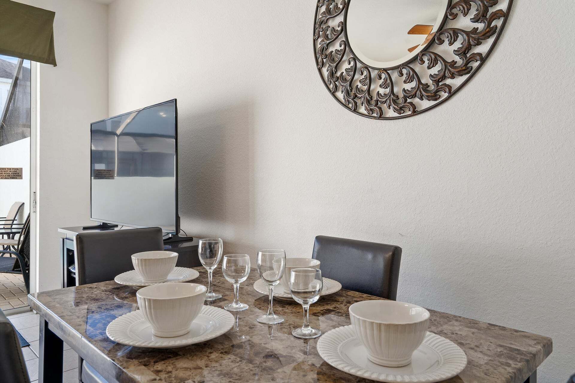 A dining area with a table set for four, a television, and a decorative mirror on the wall.
