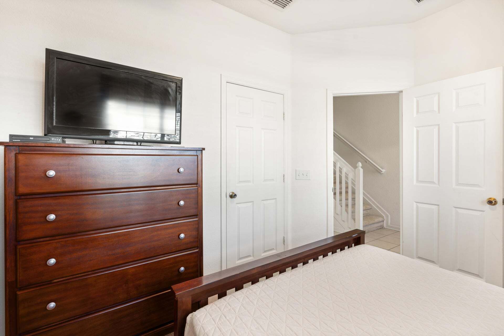 A bedroom with a wooden dresser, a bed, a television on the dresser, and white doors.