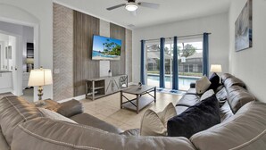 Ein Wohnzimmer mit einer Couch, einem Fernseher, einem Deckenventilator und Blick auf einen Swimmingpool.