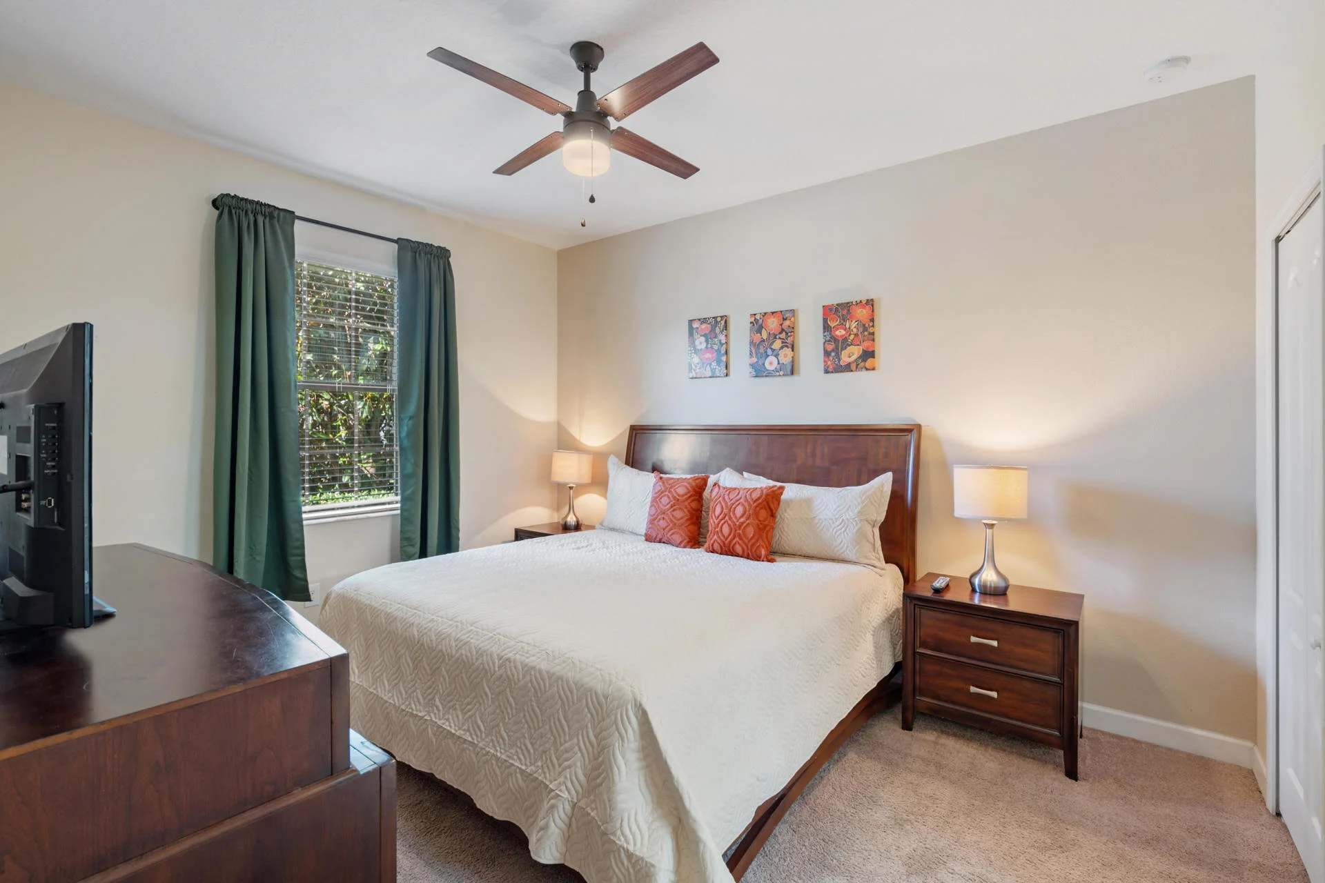 A hotel room with a bed, bedside tables, a ceiling fan, and artwork on the wall.