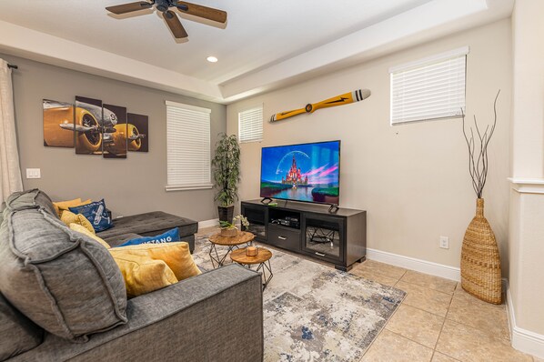 A living room with a gray sofa, a flat-screen TV, a ceiling fan, and a decorative wall piece. - Amazing Home in Davenport 4br 3.5 Bath (Davenport)