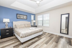 A bedroom with a tufted headboard bed, two bedside tables with lamps, a large mirror, and a ceiling fan. - Amazing Home in Davenport 4br 3.5 Bath (Davenport)
