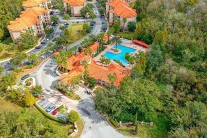 An aerial view of a resort with multiple buildings, a swimming pool, and a parking area surrounded by greenery. - Amazing Home in Davenport 4br 3.5 Bath (Davenport)