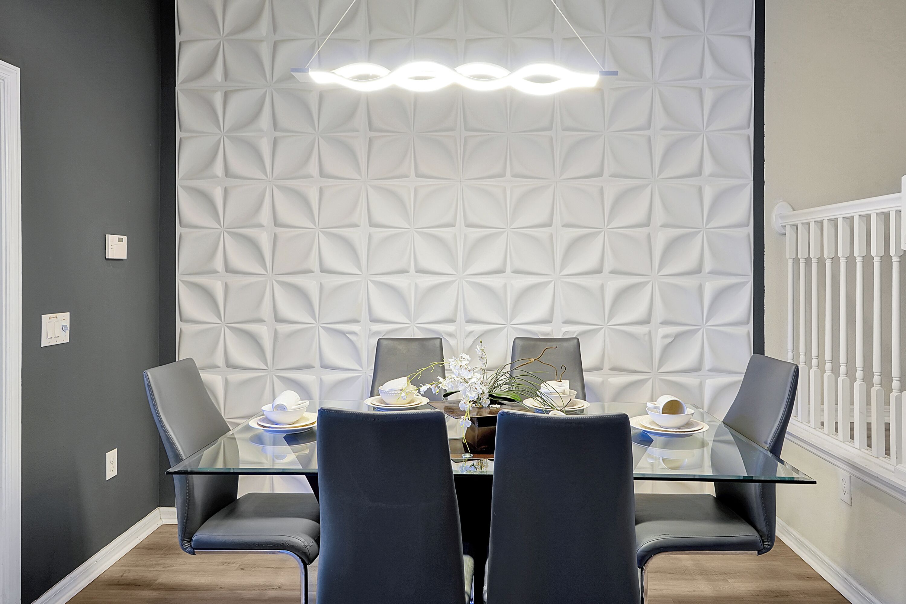 A dining area with a glass table, dark chairs, and a textured wall behind.