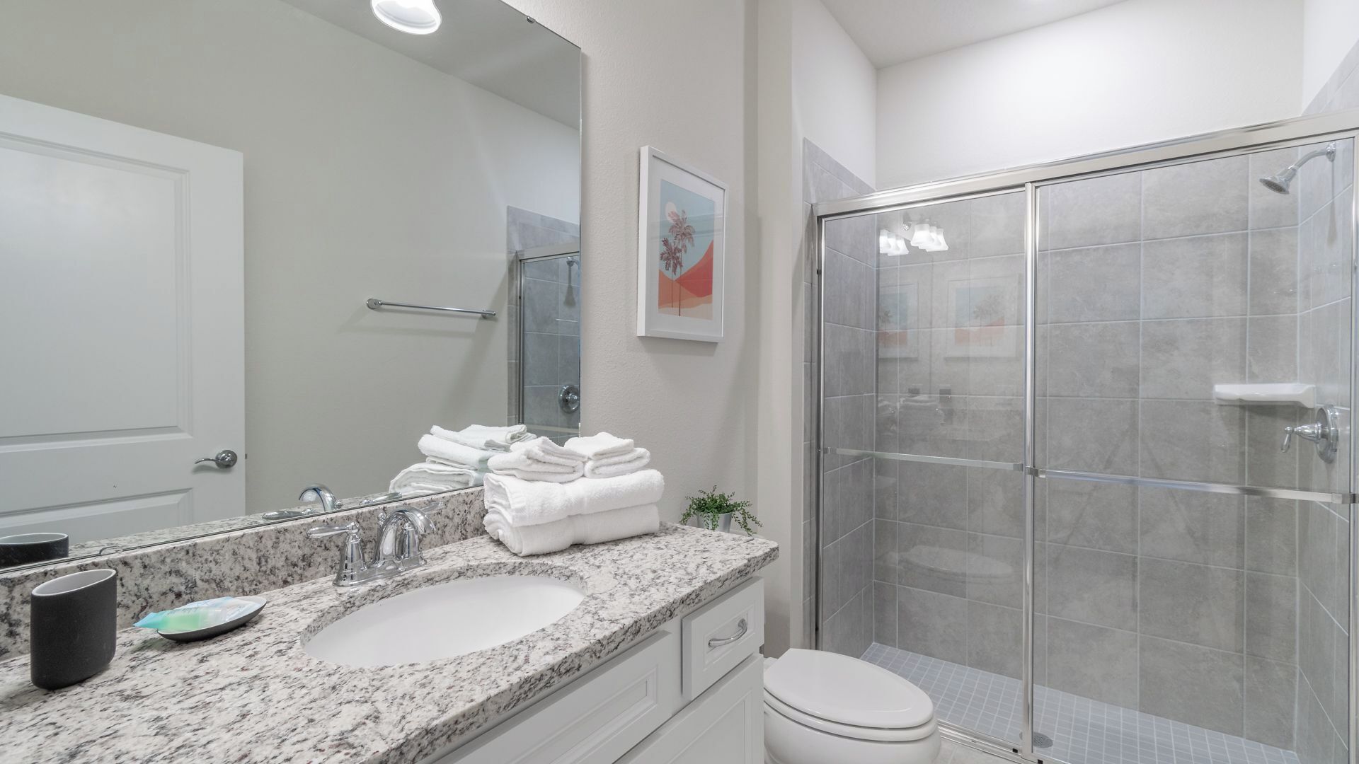 A modern bathroom with a granite countertop sink, a glass shower enclosure, and a white toilet.
