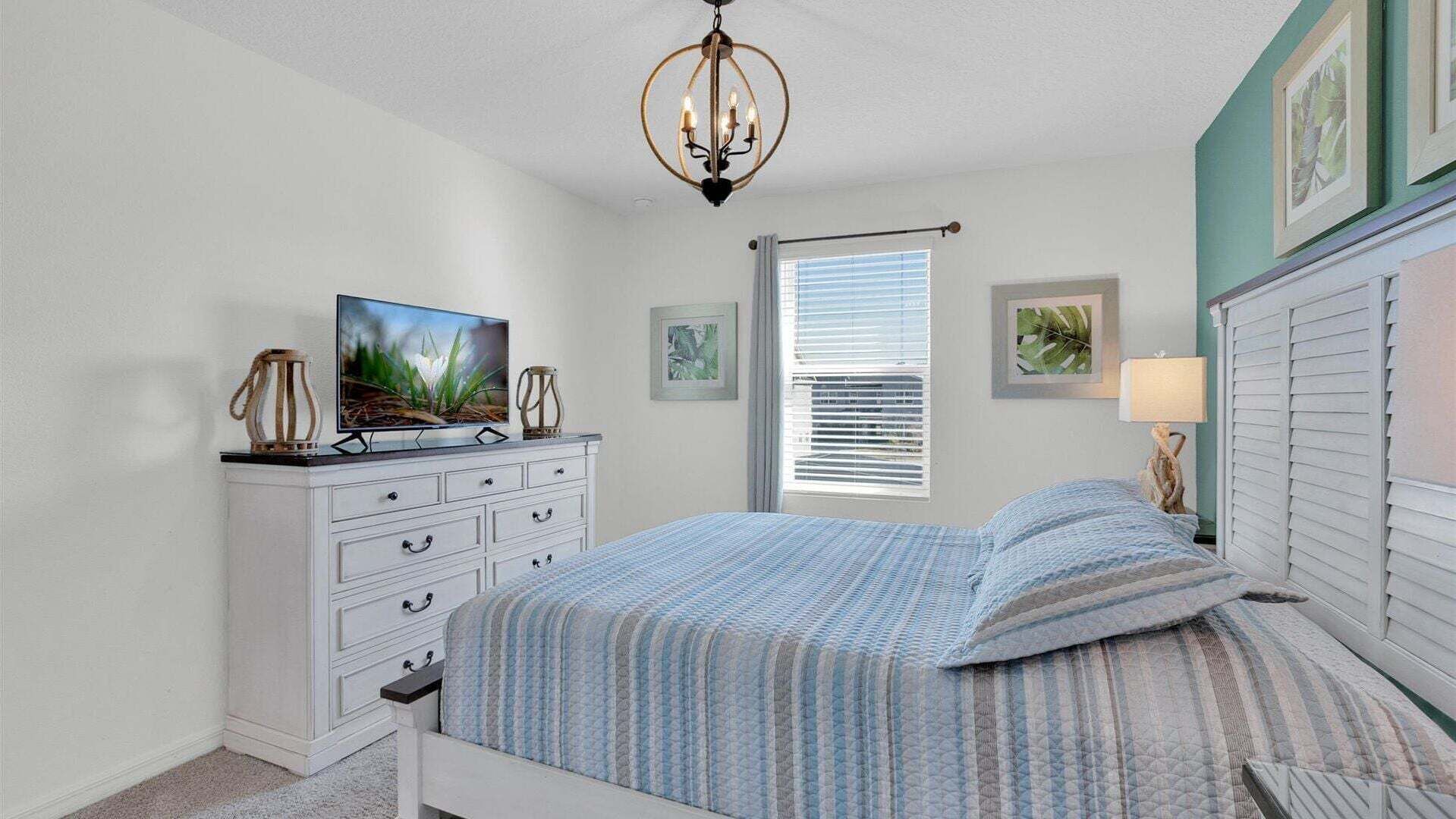 A bedroom with a bed, a dresser, a television, and a window with blinds.